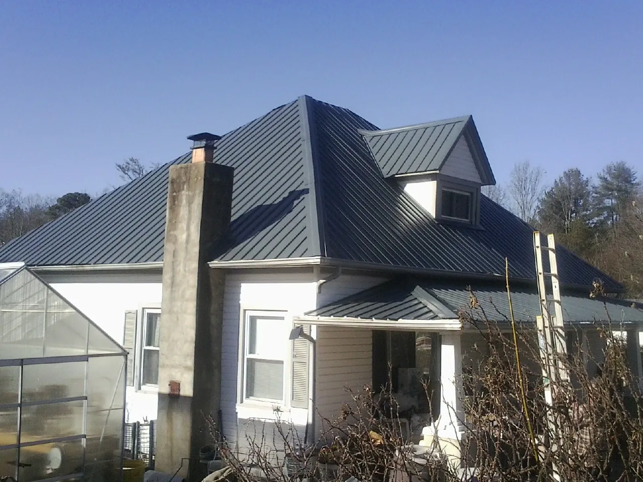 Dark blue standing seam metal roof on a white farmhouse with dormer — Slate & Tile Roof Repair by Roofing Brothers in Bruin