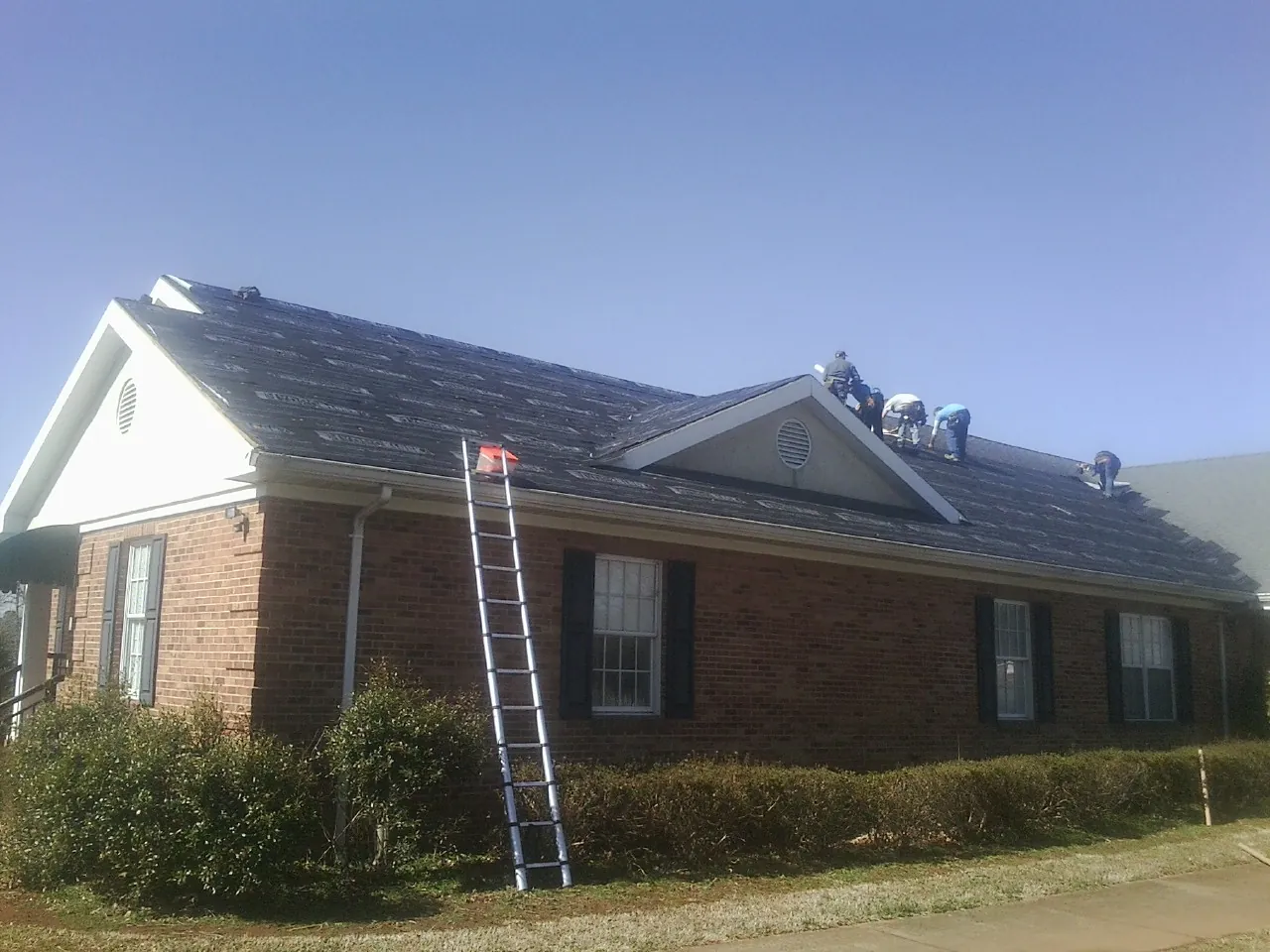 Crew tearing shingles off a brick ranch roof with a ladder set — Emergency Roof Repair work by our crew in Bruin