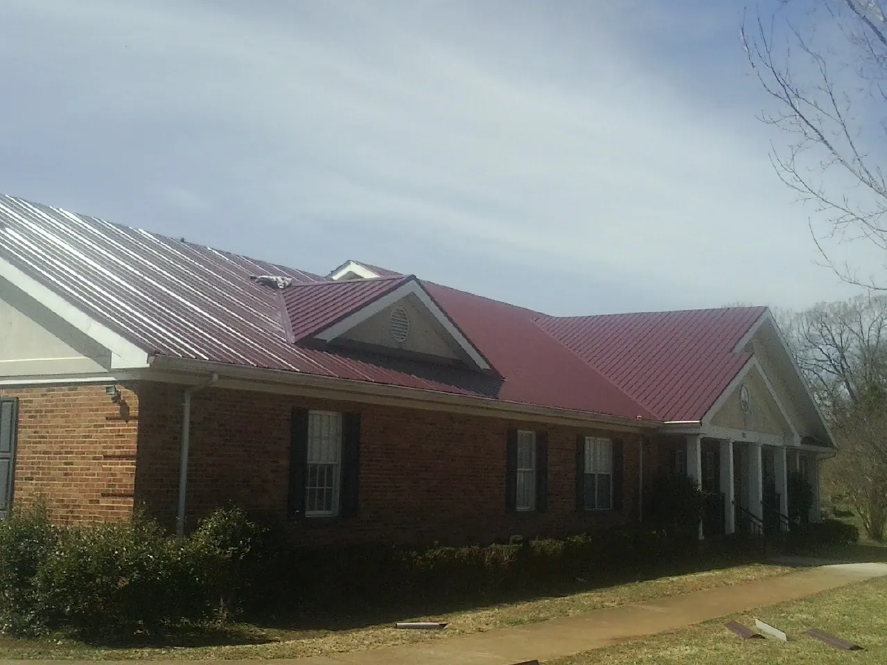 Red metal roof with gabled entries on a long brick building, from a Hail Damage Roof Repair job in Bruin