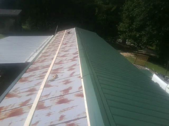 Old rusted panels beside newly installed green metal roofing — Wind Damage Roof Repair by Roofing Brothers in Bruin