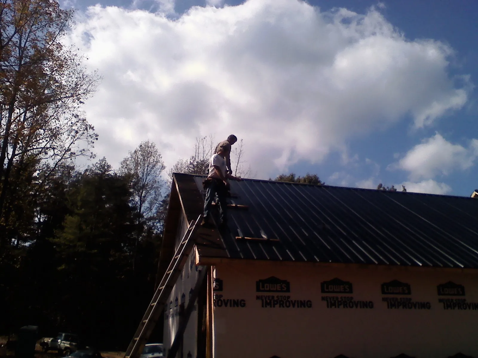 Roofer fastening dark metal panels high against a cloudy sky, from a Roof Inspection job in Bruin