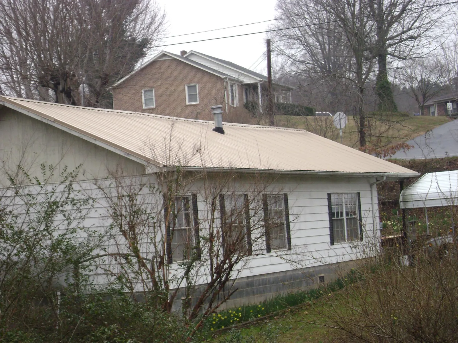Tan metal roof on a white sided house set into a hillside — Commercial Roofing by Roofing Brothers in Bruin